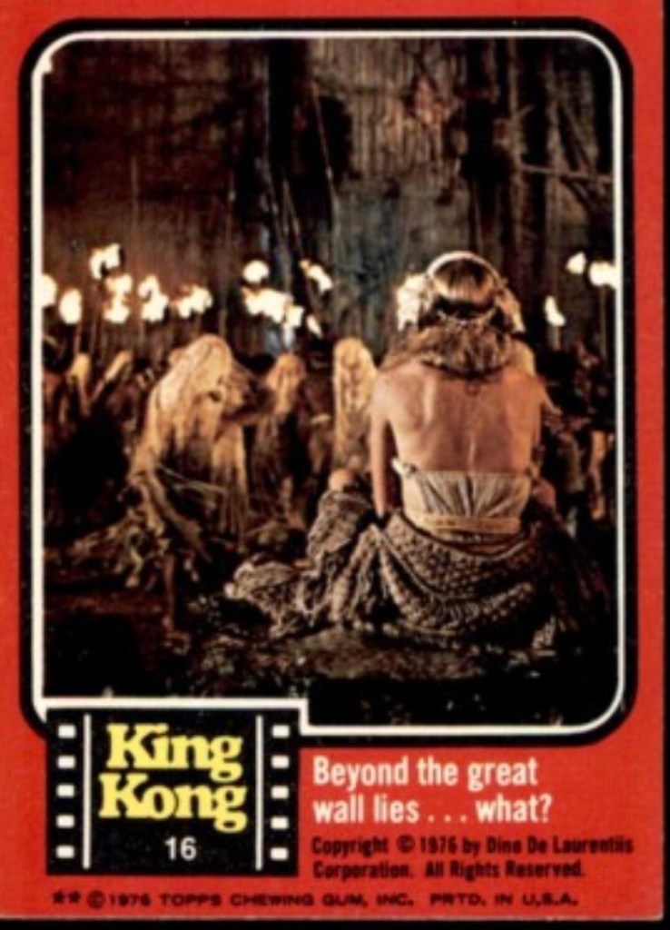 A vintage trading card from the 1976 film King Kong featuring a woman seated with her back to the viewer, surrounded by torch-carrying figures in a dark setting, with the text 'Beyond the great wall lies... what?'
