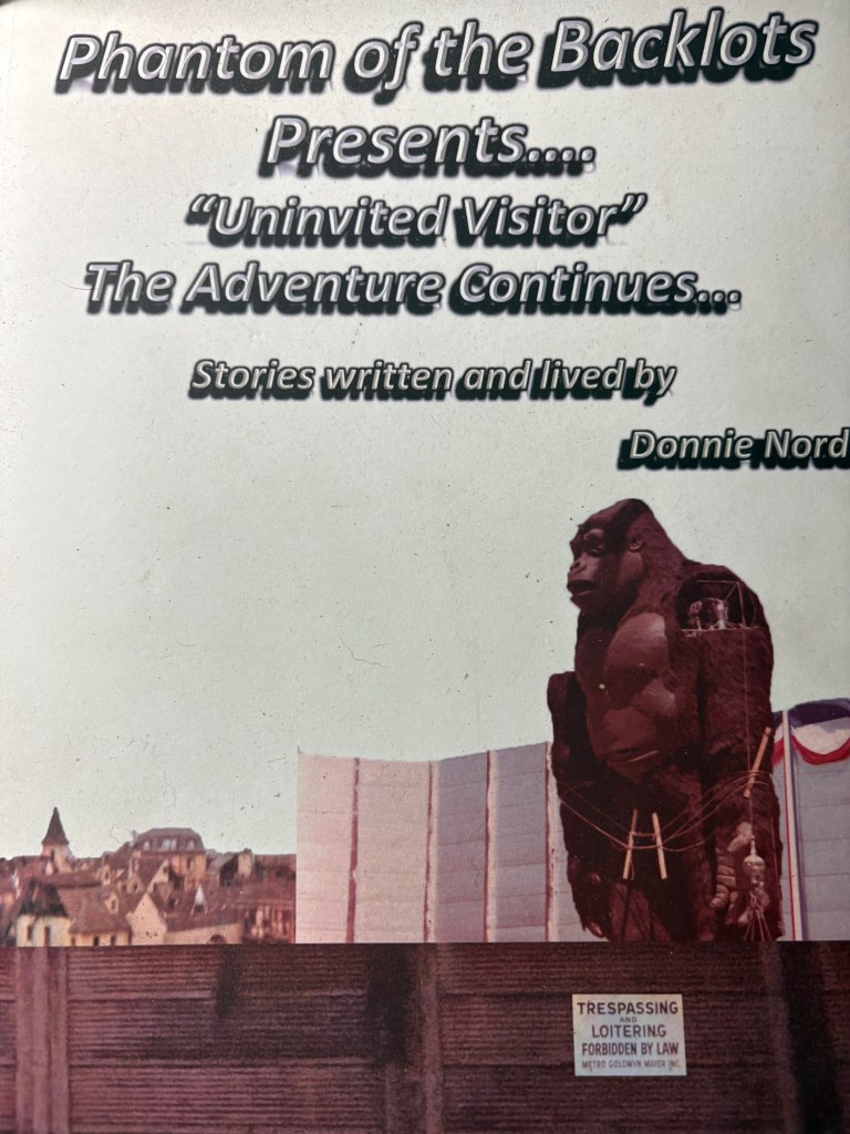 Cover of a fictional book titled 'Phantom of the Backlots Presents.... Uninvited Visitor: The Adventure Continues...' featuring a large gorilla statue in front of a backdrop of a cityscape.