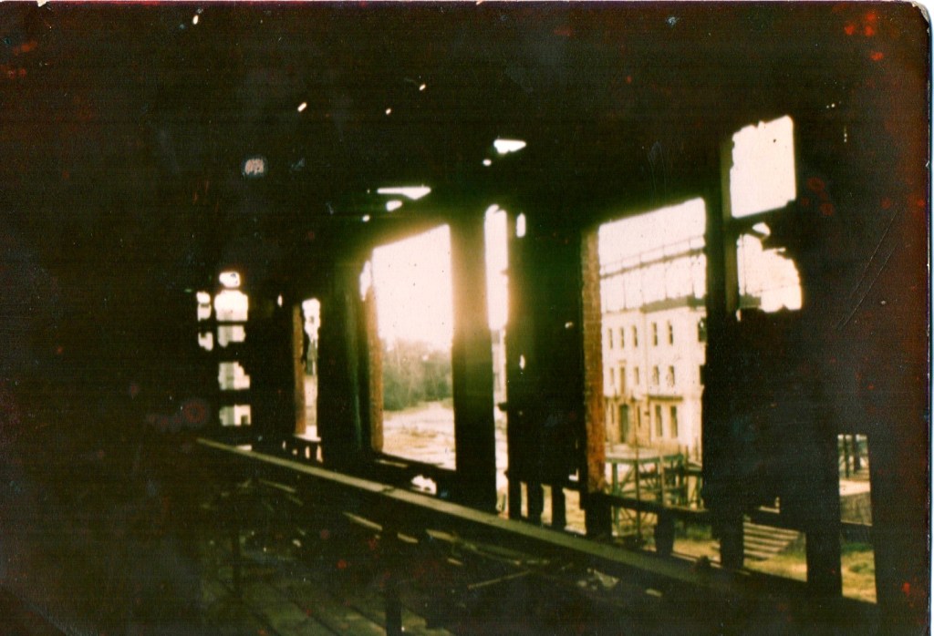 Interior view of a dilapidated building, showcasing broken windows and beams with sunlight streaming through, illuminating the dusty space.