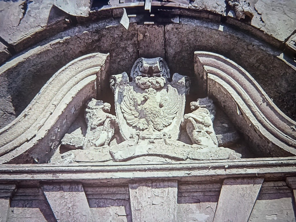 A detailed stone relief featuring an eagle and two figures on either side, with ornate decorative elements above and below.