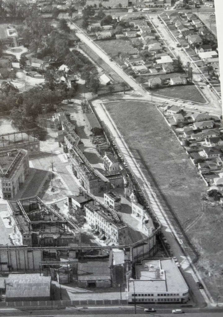Aerial view of a complex with multiple buildings, surrounded by residential homes and roads.