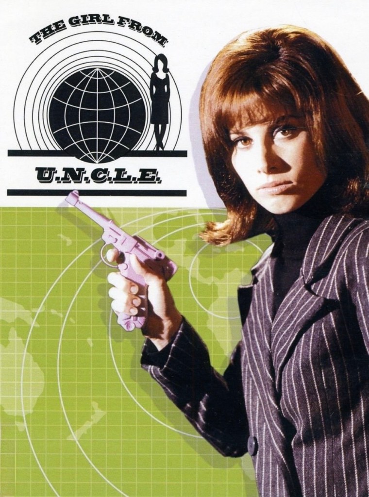 A female character from 'The Girl from U.N.C.L.E.' holds a pink toy gun, wearing a black turtleneck and a pinstripe suit, set against a green background with a globe graphic.