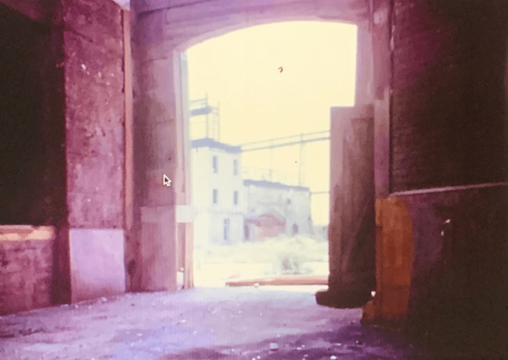 View of an industrial archway leading to an outdoor area, with distant buildings visible through the opening.